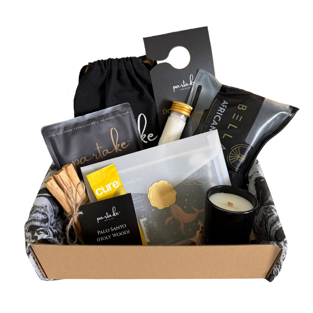 Gift box with various items including a candle, packaging, and a black bag on a white background